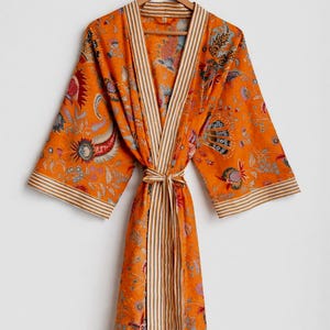 May include: An orange floral print robe with a striped trim and matching belt. The robe is hanging on a wooden hanger. The floral pattern includes red, blue, and green accents.