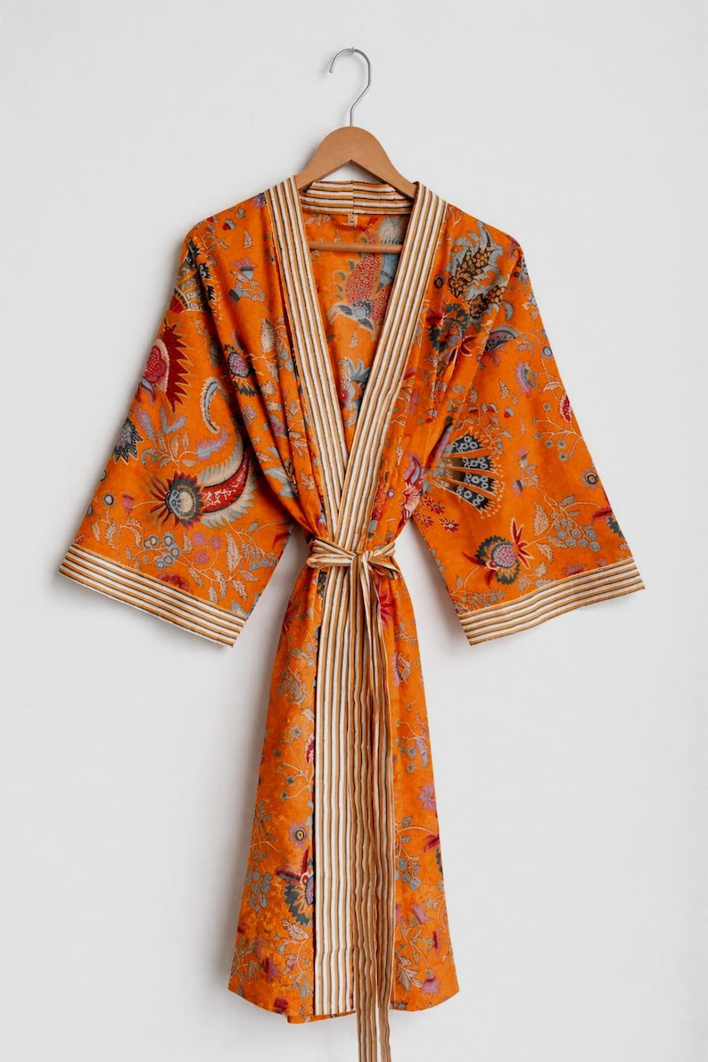 May include: An orange floral print robe with a striped trim and matching belt. The robe is hanging on a wooden hanger. The floral pattern includes red, blue, and green accents.