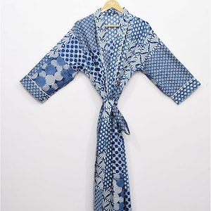 May include: A blue and white patterned robe with a tie closure, hanging on a wooden hanger. The robe features various geometric and floral designs. The robe is made of a lightweight fabric.