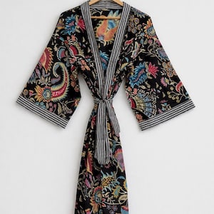 May include: A black floral print robe with a striped trim and tie. The robe features a colorful paisley and floral design in shades of red, blue, yellow, and pink. The robe is hanging on a wooden hanger.