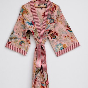 May include: A pink floral print robe with a striped trim and belt. The robe features a V-neck design and long sleeves. The floral pattern includes blue, red, and yellow accents. The robe is hanging on a wooden hanger.