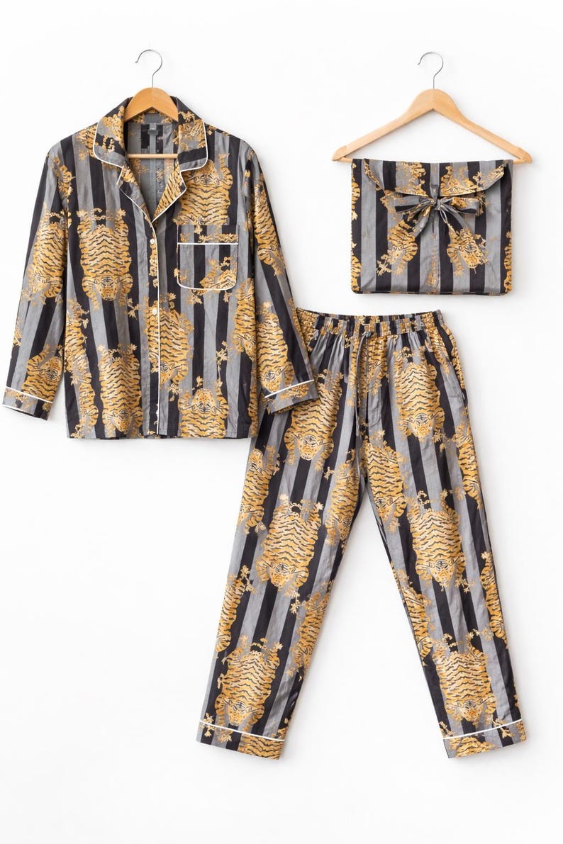 May include: A matching pajama set featuring a button-down shirt, pants, and a storage pouch. The set is patterned with vertical black and gray stripes and gold tiger illustrations. White trim accents the shirt and pants.
