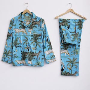 Puede incluir: Conjunto de pijama azul claro con estampado de animales tropicales. El conjunto incluye una camisa con botones y pantalones a juego. El estampado presenta cebras, leopardos, tucanes y palmeras. La camisa tiene un bolsillo en el pecho.