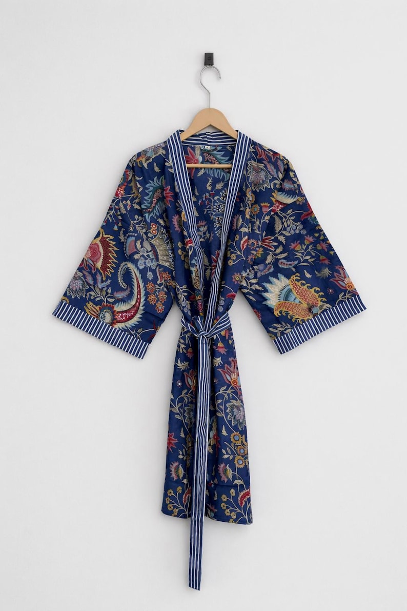 May include: A navy blue robe with a floral pattern in red, yellow, and green. The robe has white and blue striped trim on the collar and sleeves. A matching belt is tied at the waist. The robe is hanging on a wooden hanger.