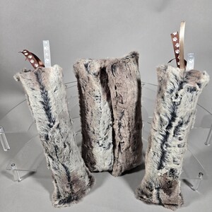 May include: Three plush, faux fur pet toys in shades of gray and brown. Two are cylindrical, and one is rectangular. Each toy has a ribbon with paw print accents.