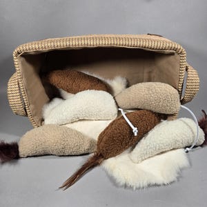 May include: A woven basket overflowing with plush cat toys. The toys are shaped like mice and are in various shades of brown, cream, and white. Some have feather tails. The basket is tan and brown.
