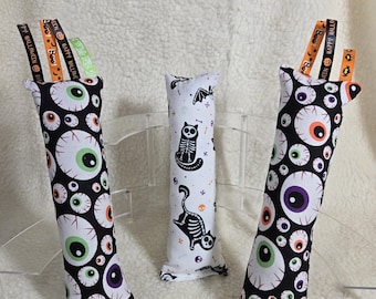 May include: Three Halloween-themed cat toys. Two are black with eyeball patterns, and one is white with a skeleton cat design. Each toy has a ribbon with "Happy Halloween" text.