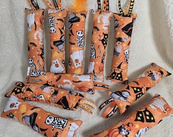 May include: Orange Halloween-themed cat toys with various spooky designs, including ghosts, skeletons, and cats in witch hats. Some toys have orange ribbons with the text "Boo!" and "Happy Halloween". The toys are made of fabric and filled with stuffing.