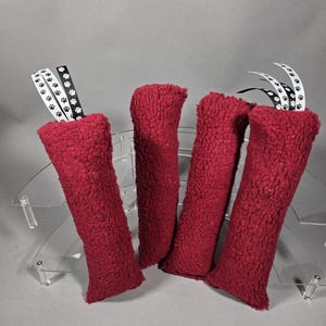 May include: Four red plush cat toys are displayed, each with a rectangular shape and a textured surface. White ribbons with black paw prints are attached to two of the toys. The toys are arranged on a clear, tiered display.