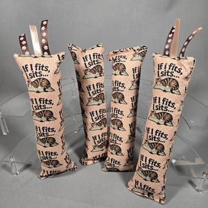 May include: Four cat toys with a light pink background, patterned with a sleeping cat and the text "If I fits, I sits...". Each toy has a ribbon accent at the top. These cat toys are designed to entertain your feline friend.