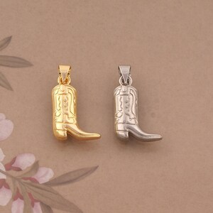 May include: Two metal pendants shaped like cowboy boots, one with a polished gold-tone finish and the other with a polished silver-tone finish. Each boot features embossed decorative stitching patterns and a small metal loop at the top for hanging.