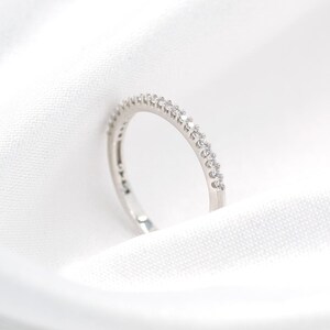 May include: A thin silver-toned band ring featuring a row of small, clear, round-cut stones set along the top half of the exterior. The metal has a polished, reflective finish, and the stones are arranged in a continuous, uniform line.