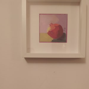 Puede incluir: Una pintura enmarcada de una granada roja sobre un fondo amarillo con un cielo morado y rosa.