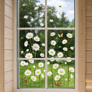 May include: A window with white daisies and green leaves stickers. The daisies have yellow centers and white petals. Orange butterflies are also included in the design. The window is framed by a white grid and a wooden frame.