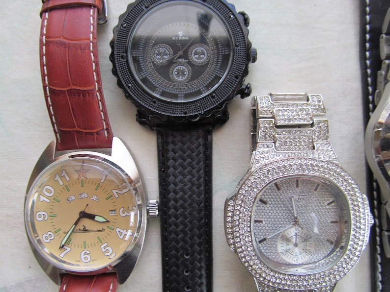May include: Three wristwatches with different styles and designs. The first watch has a brown leather band and a round face with a beige background. The second watch has a black band with a textured pattern and a round face with a black background. The third watch has a silver band with a diamond-like pattern and a round face with a white background.