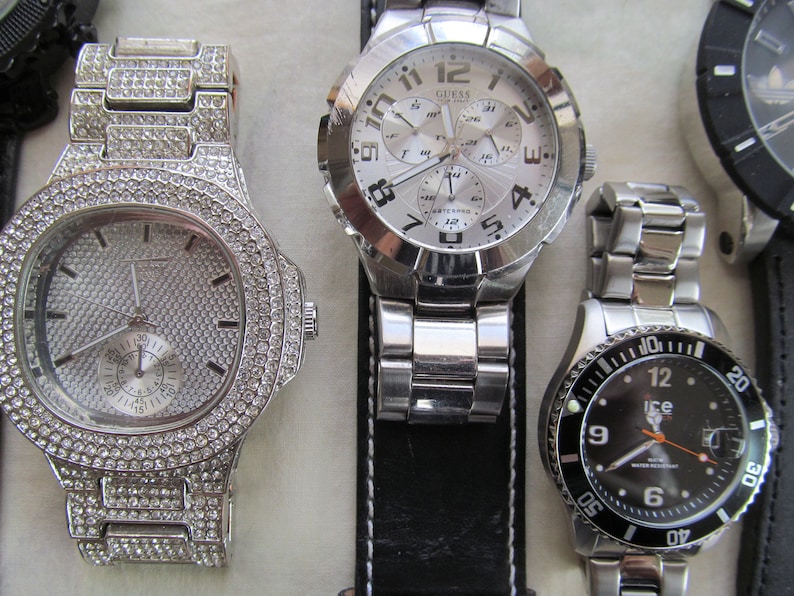 May include: Four wristwatches with silver and black bands. The watch on the left has a silver face with a diamond-like design. The watch in the center has a silver face with black numbers and hands. The watch on the right has a black face with silver numbers and hands. The watch in the background has a black face with silver hands.