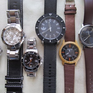 May include: A collection of six wristwatches with different styles and designs. The watches feature various band materials, including leather, metal, and wood. Some of the watches have a silver or gold tone, while others have a black or brown tone.