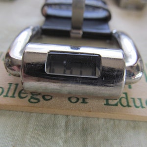 May include: A silver-toned digital watch with a black face and a black leather band. The watch face displays the time as 11:11.