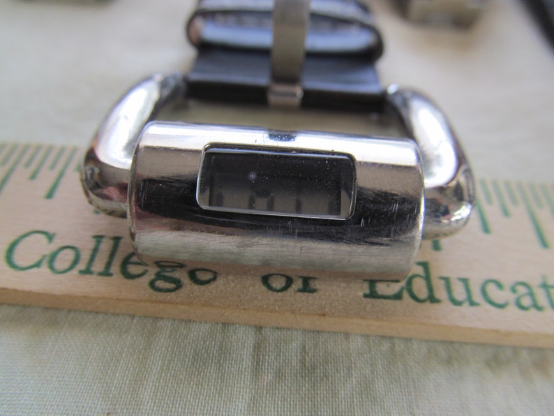 May include: A silver-toned digital watch with a black face and a black leather band. The watch face displays the time as 11:11.