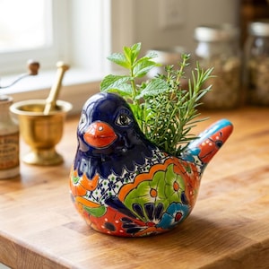 May include: A colorful ceramic bird planter with a blue head, orange beak, and vibrant floral patterns in orange, green, and blue. The bird holds fresh herbs, including mint and rosemary, making it a decorative kitchen accent.