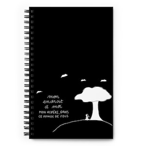 Peut inclure: Cahier à spirales noir avec une illustration fantaisiste. La couverture présente une forme blanche en forme d'arbre, une petite silhouette et le texte manuscrit "mon endroit à moi, mon repère, dans ce monde de fous."