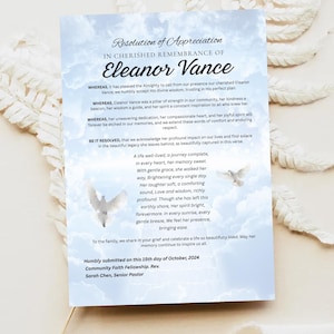 May include: A memorial card with a light blue sky and cloud design. The card features text in a formal script, including the name "Eleanor Vance" and a poem. Two white dove illustrations are also present.