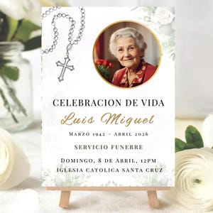 May include: A memorial sign featuring a portrait of an elderly woman in a gold frame. The sign has Spanish text: "CELEBRACION DE VIDA Luis Miguel" with dates and service information. A rosary and floral elements decorate the design.