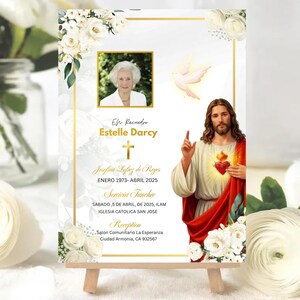 May include: A memorial card with a photo of a woman, floral accents, and a gold border. The card includes text in Spanish, a photo of Jesus, and a dove illustration. The card is displayed on a small wooden easel.