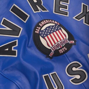 May include: Close-up of a royal blue leather jacket with white and black lettering. The jacket features a patch with the American flag and the words "ALL AMERICANS ESTABLISHED 1975 N.Y."