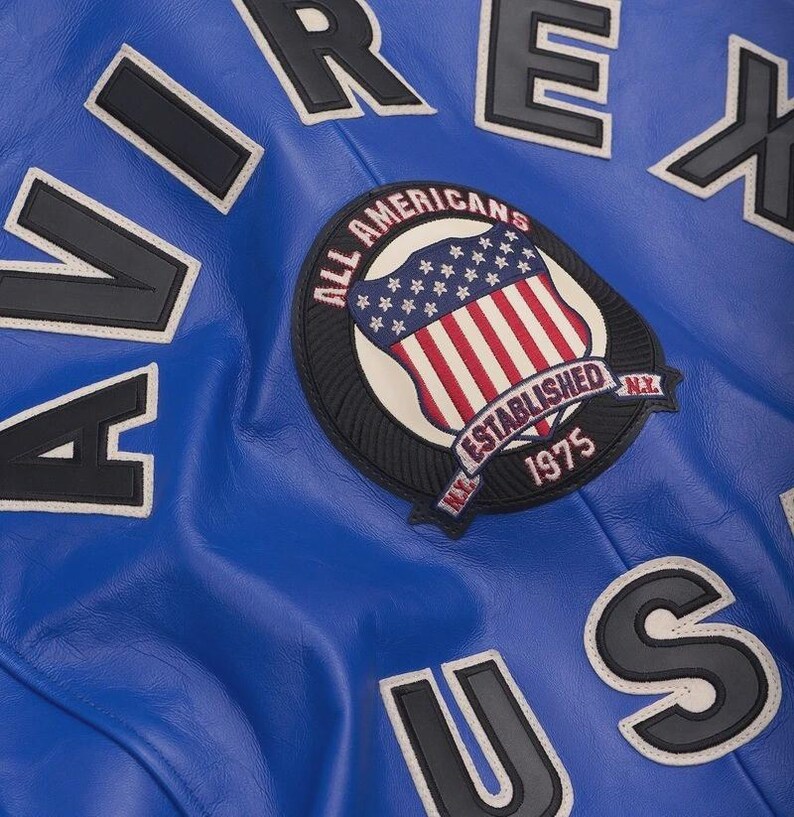 May include: Close-up of a royal blue leather jacket with white and black lettering. The jacket features a patch with the American flag and the words "ALL AMERICANS ESTABLISHED 1975 N.Y."