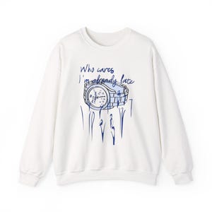 May include: White crew neck sweatshirt with a blue graphic of a watch and the text "Who cares I'm already late". The watch graphic has a blue outline and the text is in a handwritten style.