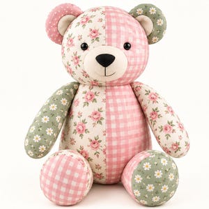 Puede incluir: Un oso de peluche hecho de tela de retazos con patrones alternos de rosas rosadas sobre crema, cuadros vichy rosas y blancos, y margaritas blancas sobre un fondo verde salvia. El oso tiene ojos de plástico negro y una nariz negra cosida.