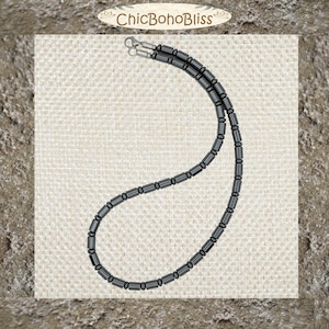 May include: A necklace composed of smooth, cylindrical, dark gray metallic beads strung together in a continuous loop. The piece features a silver-toned metal lobster claw clasp at the top, providing a secure closure for this simple, uniform jewelry item.