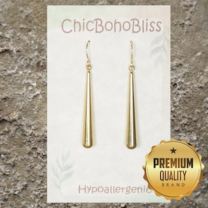 May include: A pair of gold-toned drop earrings with a smooth, tapered, cylindrical design suspended from thin hooks. The earrings are displayed on a white card featuring the text ChicBohoBliss and Hypoallergenic, with a gold premium quality seal.