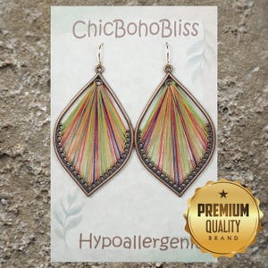 May include: A pair of teardrop-shaped earrings featuring a copper-toned metal frame with intricate thread-wrapped detailing in vibrant shades of green, orange, purple, and yellow. The earrings are displayed on a card labeled ChicBohoBliss.