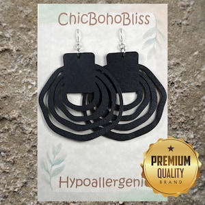 May include: A pair of black earrings featuring a rectangular top piece connected to three concentric, wavy, circular cutouts. The earrings are displayed on a white card labeled ChicBohoBliss and Hypoallergenic, with a gold Premium Quality Brand seal.
