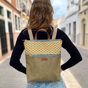 Peut inclure: Un sac à dos en toile vert avec une poche zippée à motif jaune et blanc. Le sac à dos a une poignée en cuir marron et des bretelles réglables.