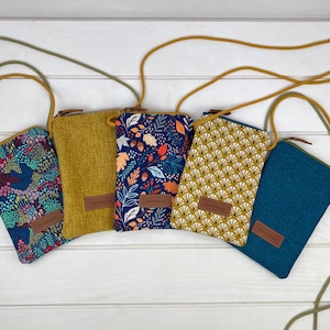 Può includere: Cinque diverse pochette per telefono con cinturini regolabili. Le pochette sono realizzate in tessuto e presentano vari motivi, tra cui floreali, geometrici e tinta unita. Le pochette sono tutte in una gamma di colori giallo senape.
