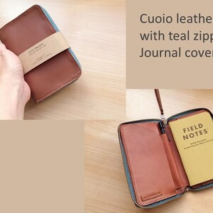 May include: A brown leather journal cover with a teal zipper closure. The cover features a paper band with the text 'Cuoio leather with teal zipper Journal cover'. The interior includes a tan Field Notes memo book and a black pen holder.