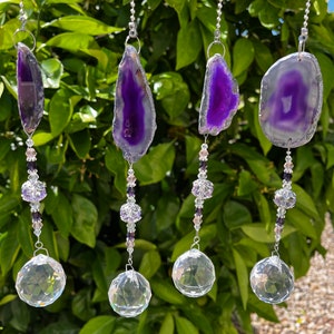 May include: Four hanging suncatchers featuring purple agate slices at the top, connected by strings of small clear and purple beads, and ending with a large, multifaceted clear crystal sphere at the bottom, all suspended by silver chains.