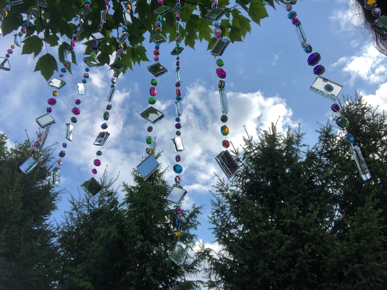 Beautiful hanging strings adorned with mirrors and colorful rhinestones that will hang from low tree branches.  They dangle freely and will move with the breeze, casting whimsical reflections throughout your outdoor space.  Whimsical colorful art