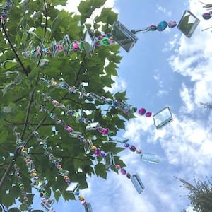 Beautiful hanging strings adorned with mirrors and colorful rhinestones that will hang from low tree branches.  They dangle freely and will move with the breeze, casting whimsical reflections throughout your outdoor space.  Whimsical colorful art
