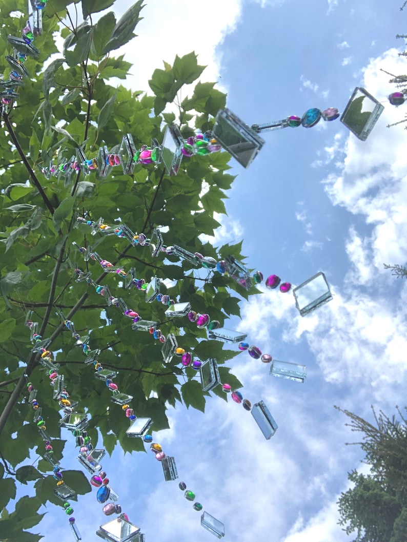 Beautiful hanging strings adorned with mirrors and colorful rhinestones that will hang from low tree branches.  They dangle freely and will move with the breeze, casting whimsical reflections throughout your outdoor space.  Whimsical colorful art