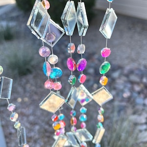 Puede incluir: M&oacute;vil decorativo colgante con hilos de cuentas de colores y detalles de diamantes espejados. Las cuentas son de varios colores, incluyendo rosa, azul, verde y amarillo. El m&oacute;vil est&aacute; dise&ntilde;ado para captar la luz y crear un efecto brillante.