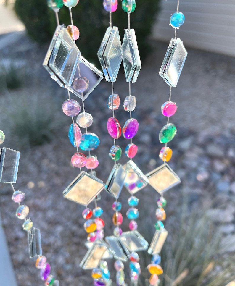 Puede incluir: M&oacute;vil decorativo colgante con hilos de cuentas de colores y detalles de diamantes espejados. Las cuentas son de varios colores, incluyendo rosa, azul, verde y amarillo. El m&oacute;vil est&aacute; dise&ntilde;ado para captar la luz y crear un efecto brillante.