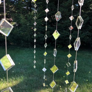 May include: Multiple vertical strands of clear, diamond-shaped glass mirror pieces connected by thin silver-toned wire. The reflective geometric shapes vary in size and are spaced along each string, creating a hanging decorative mobile display.