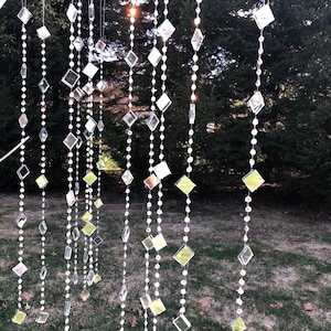 Puede incluir: Múltiples hilos verticales de cuentas de cristal transparente facetadas intercaladas con pequeños espejos reflectantes de forma cuadrada y de diamante. Los hilos cuelgan de una rama, creando una exhibición brillante de luz y formas.