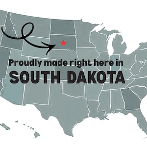 Puede incluir: Un mapa de los Estados Unidos en tonos grises, con el estado de Dakota del Sur resaltado. El texto "Proudly made right here in SOUTH DAKOTA" se muestra, con una estrella roja que indica una ubicaci&oacute;n. Una flecha negra apunta a la estrella.