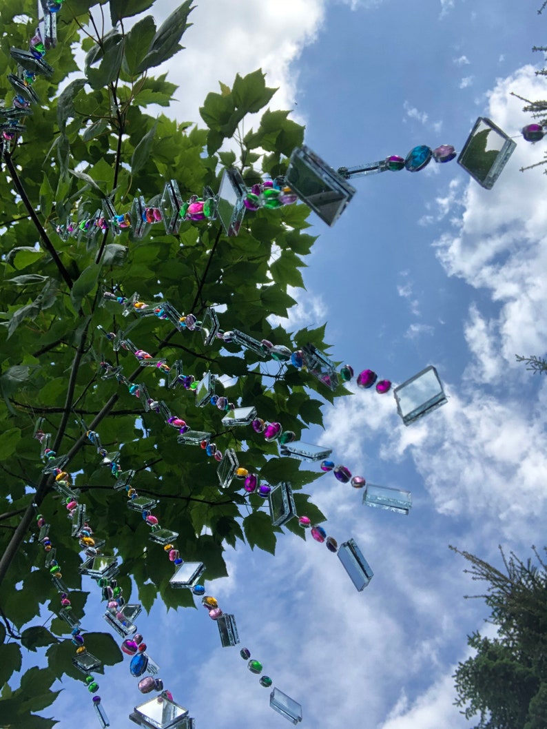 Beautiful hanging strings adorned with mirrors and colorful rhinestones that will hang from low tree branches.  They dangle freely and will move with the breeze, casting whimsical reflections throughout your outdoor space.  Whimsical colorful art