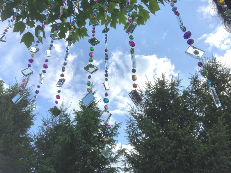 Beautiful hanging strings adorned with mirrors and colorful rhinestones that will hang from low tree branches.  They dangle freely and will move with the breeze, casting whimsical reflections throughout your outdoor space.  Whimsical colorful art